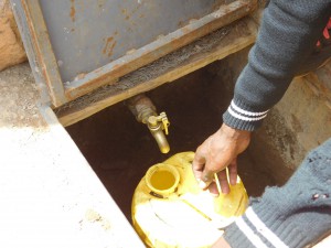 A student fills the water vessel to be used in the kitchen for the school. The spigot to the tank is accessed through a trap door at the base of the tank. This allows the spigot to be closed off so that it can’t be used without permission and it can’t be broken by students playing with it.